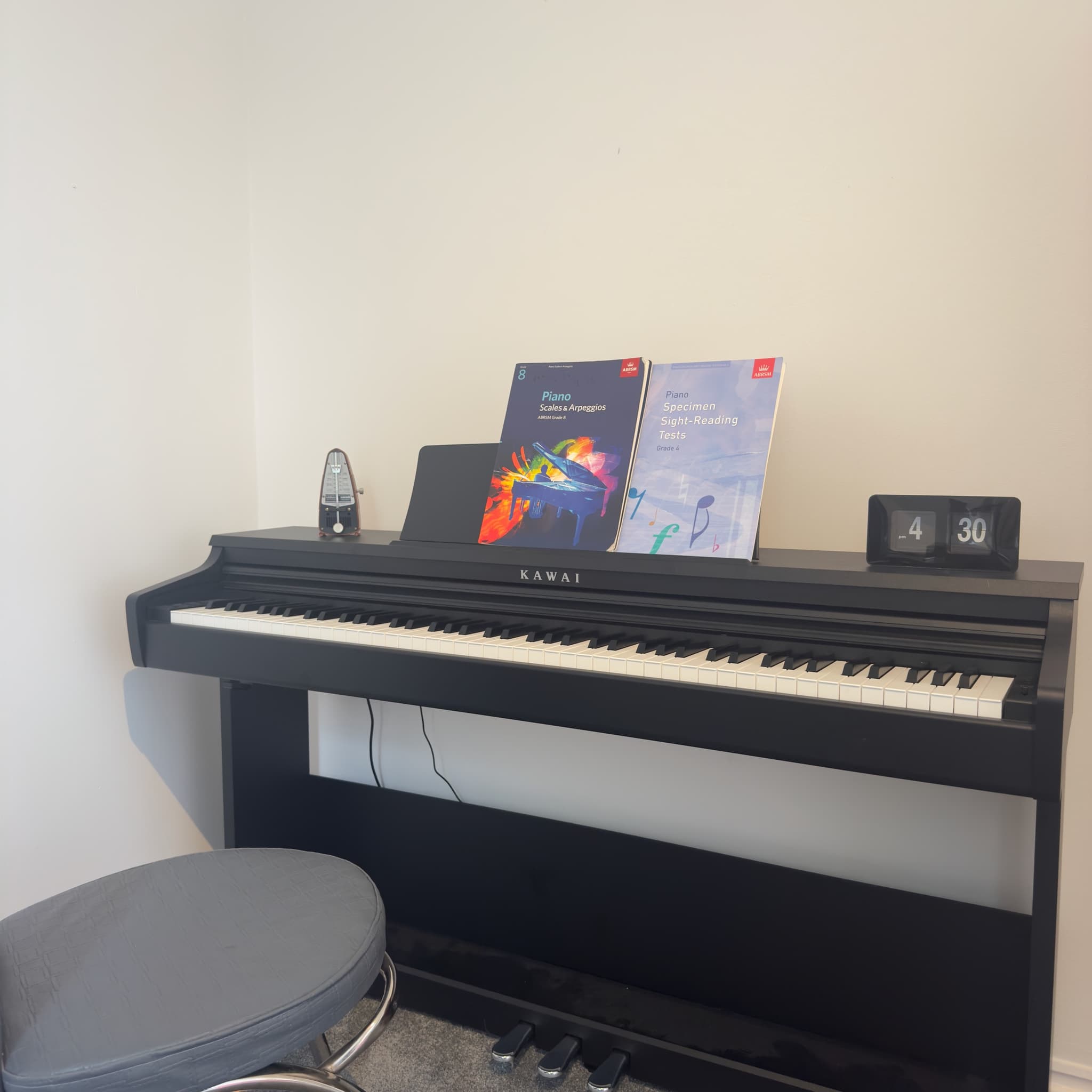 A Kawai piano set up for a one-to-one lesson, with ABRSM grade books and a metronome